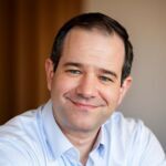 Headshot of brunette man in blue button up shirt